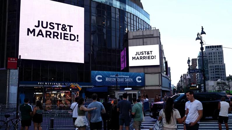 Pessoas observam telas gigantes exibindo a mensagem "JUST MARRIED!" de Taylor Swift e Travis Kelce