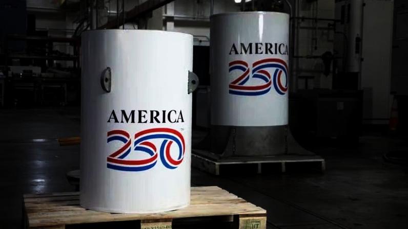 A cápsula do tempo America250 e a redoma de vidro que se encaixa sobre ela, mostradas na oficina mecânica do Instituto Nacional de Padrões e Tecnologia (NIST), onde foram criadas, em Gaithersburg, Maryland, em 2026. A redoma de vidro criará uma bolsa de ar que envolverá a cápsula e a protegerá da água em caso de inundação ou se o lençol freático no local do sepultamento subir. Juntas, as duas peças pesam aproximadamente uma tonelada