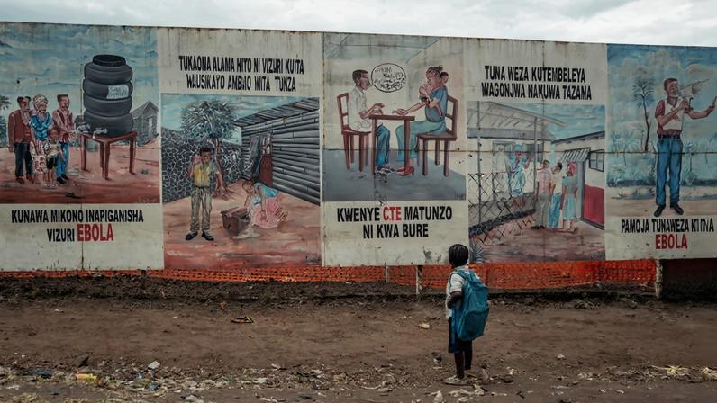 Criança voltando da escola para e observa as ilustrações de conscientização sobre o ebola em Munigi
