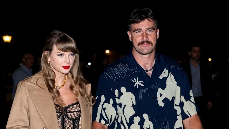 Foto colorida de mulher com batom vermelho e casaco bege de mãos dadas com homem com blusa azul estampada - Metrópoles