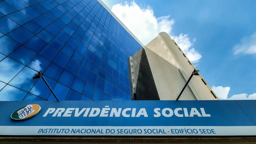 Fachada de prédio espelhado com letreiro azul escrito "Previdência Social - Instituto Nacional do Seguro Social - Edifício Sede", sob céu com nuvens.