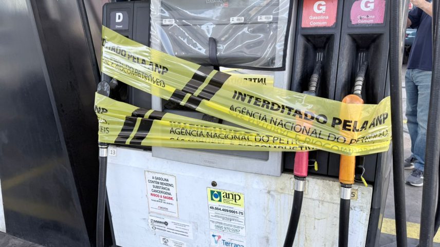 Bomba de combustível coberta por fitas amarelas com a inscrição "Interditado pela ANP", com uma pessoa ao fundo fotografando o local.