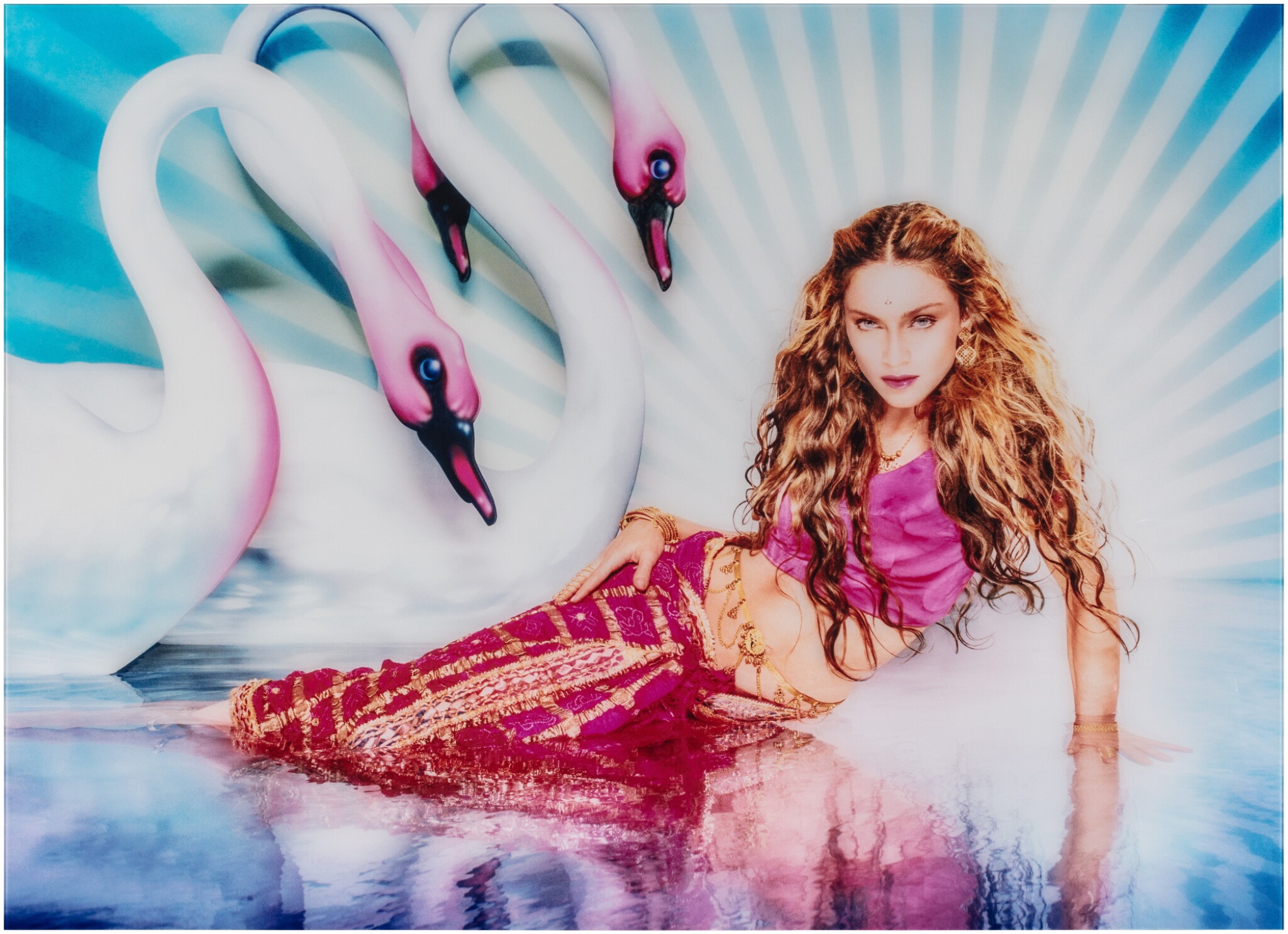 Foto de Madonna com vestes vermelhas e roxas com cores hipersaturadas enquanto três cisnes brancos a encaram com um fundo azul claro