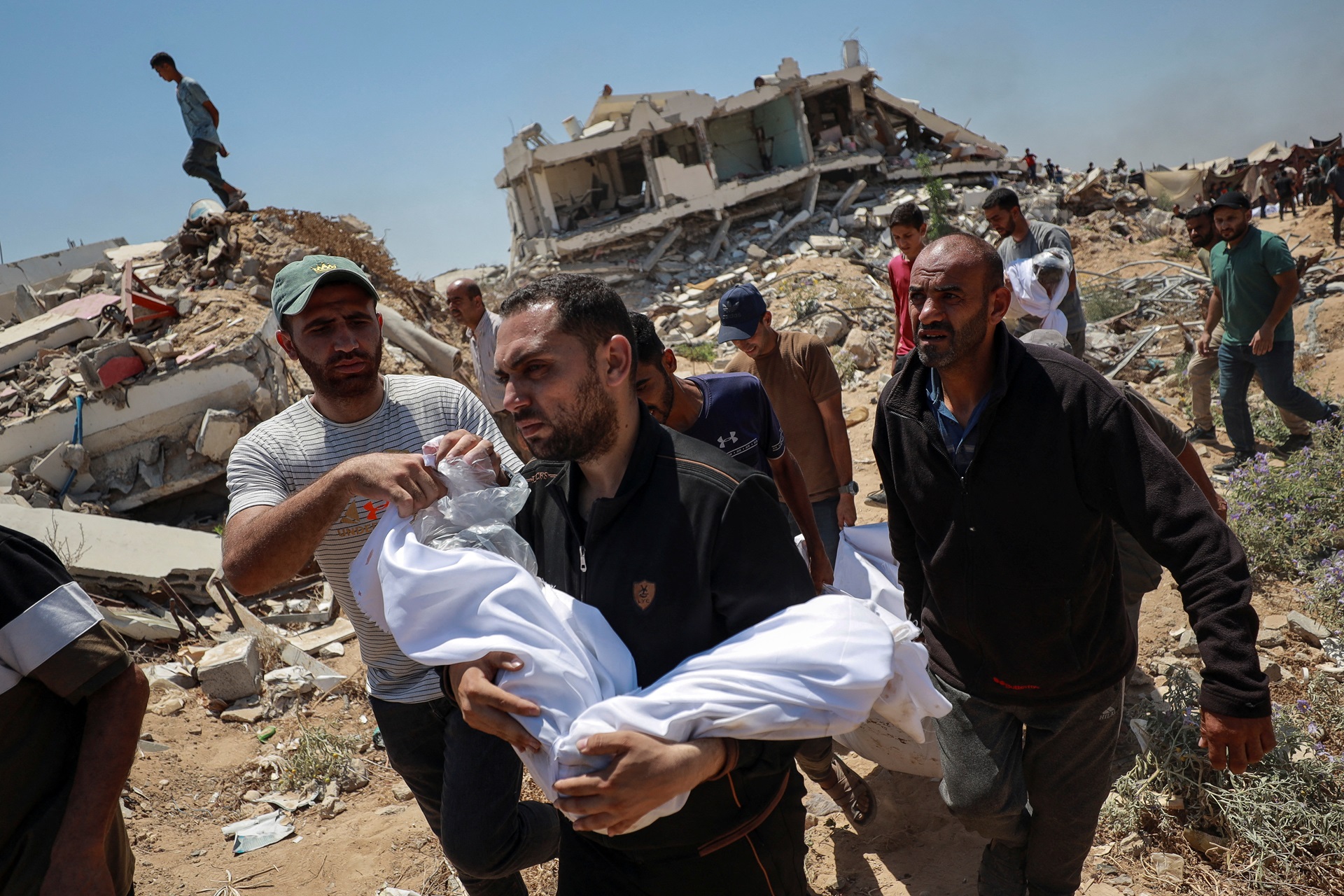 Homem carrega o corpo de uma criança durante o funeral dos palestinos da família Azzam, mortos em um ataque israelense noturno à sua casa, de acordo com médicos, antes de enterrá-los em um terreno devido à falta de espaço nos cemitérios superlotados de Gaza, na Cidade de Gaza, em 15 de julho de 2025. (Foto: REUTERS/Khamis Al-Rifi)