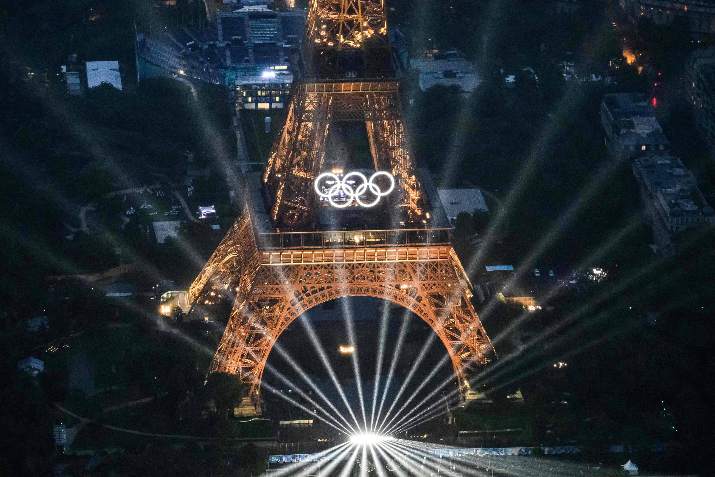 Gastos públicos de Paris-2024 chegam a R$ 37,7 bilhões Torre Eiffel iluminada à noite, com os anéis olímpicos, durante cerimônia de abertura dos Jogos de Paris (Foto: Lionel Bonaventure - 26.jul.2024/AFP)