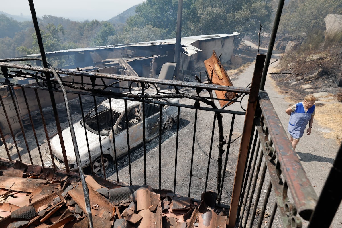 Fogo avança em Monterrei e moradores temem por suas vidas em meio ao pânico Uma mulher passava na quinta-feira frente a uma casa e um veículo queimados, em A Caridade (Ourense). (Foto: Lalo R. Villar (AP))