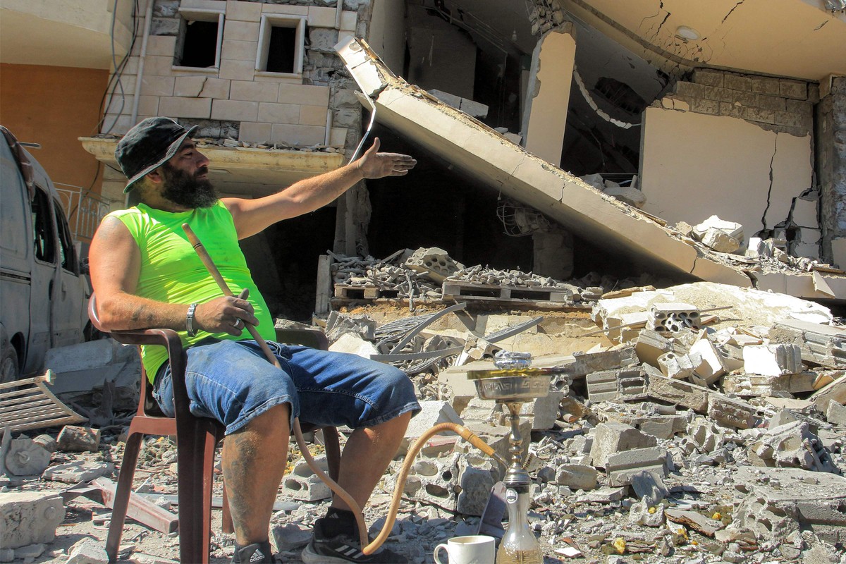 Beirute se posiciona entre as influências de Teerã e Tel Aviv Ali Mallah fuma narguilé nos escombros de seu prédio em Ain Qana, no sul do Líbano, destruído por ataque aéreo israelense (Foto: Mahmoud Zayyat/AFP)