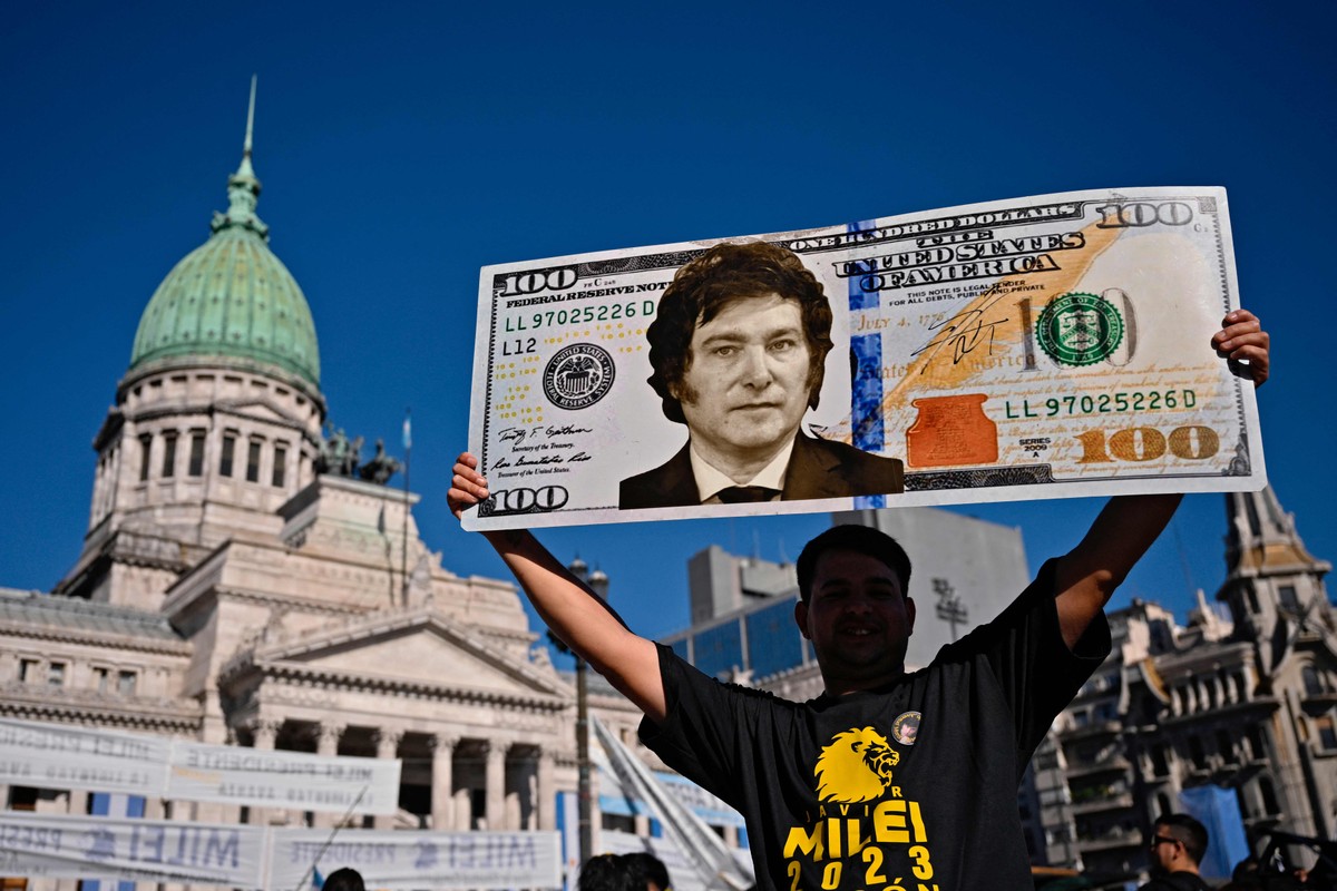 Milei enfrenta desafios para convencer argentinos a investir em dólares novamente Apoiador de Milei carrega cartaz com a foto do presidente em uma nota de dólar (Foto: Luis ROBAYO/AFP)