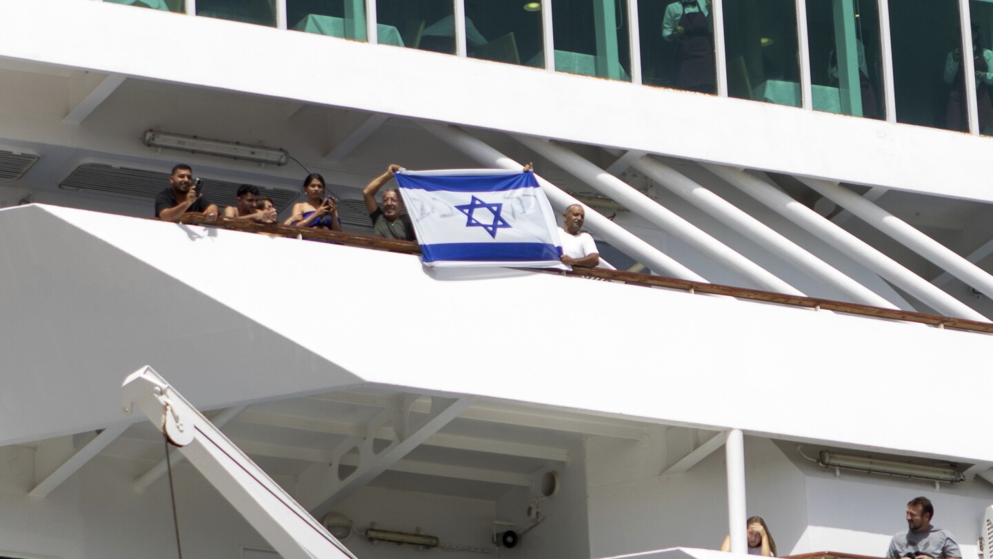 Dois homens seguram uma bandeira israelense durante a partida de um navio de cruzeiro com turistas israelenses na ilha grega de Rodes, no sudeste do Mar Egeu, na segunda-feira, 28 de julho de 2025. (Foto: InTime News via AP)