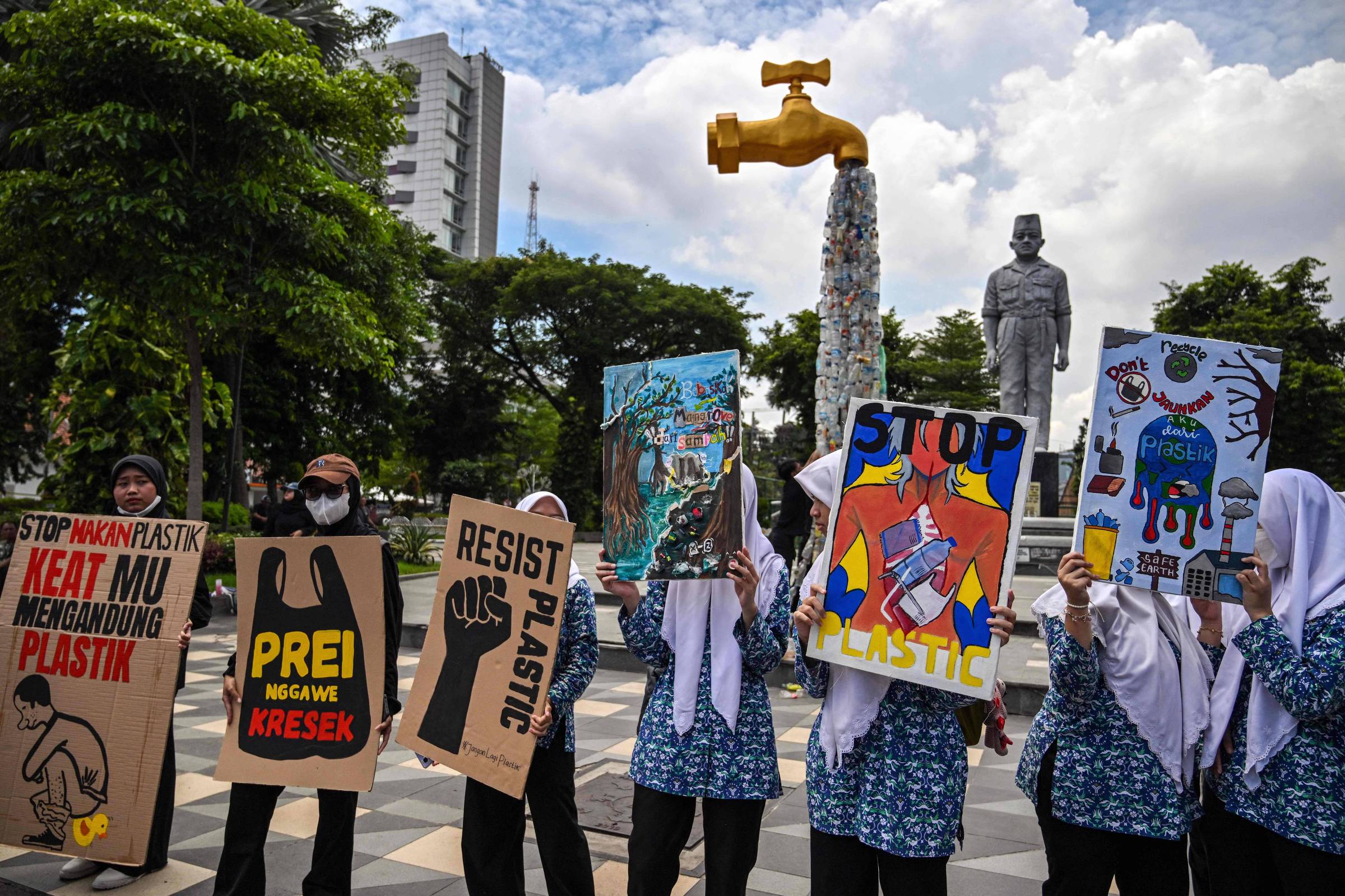Ativistas protestam contra poluição diante de instalação que mostra uma torneira da qual saem embalagens plásticas em Surabaya, na Indonésia (Foto: Juni Kriswanto/AFP)