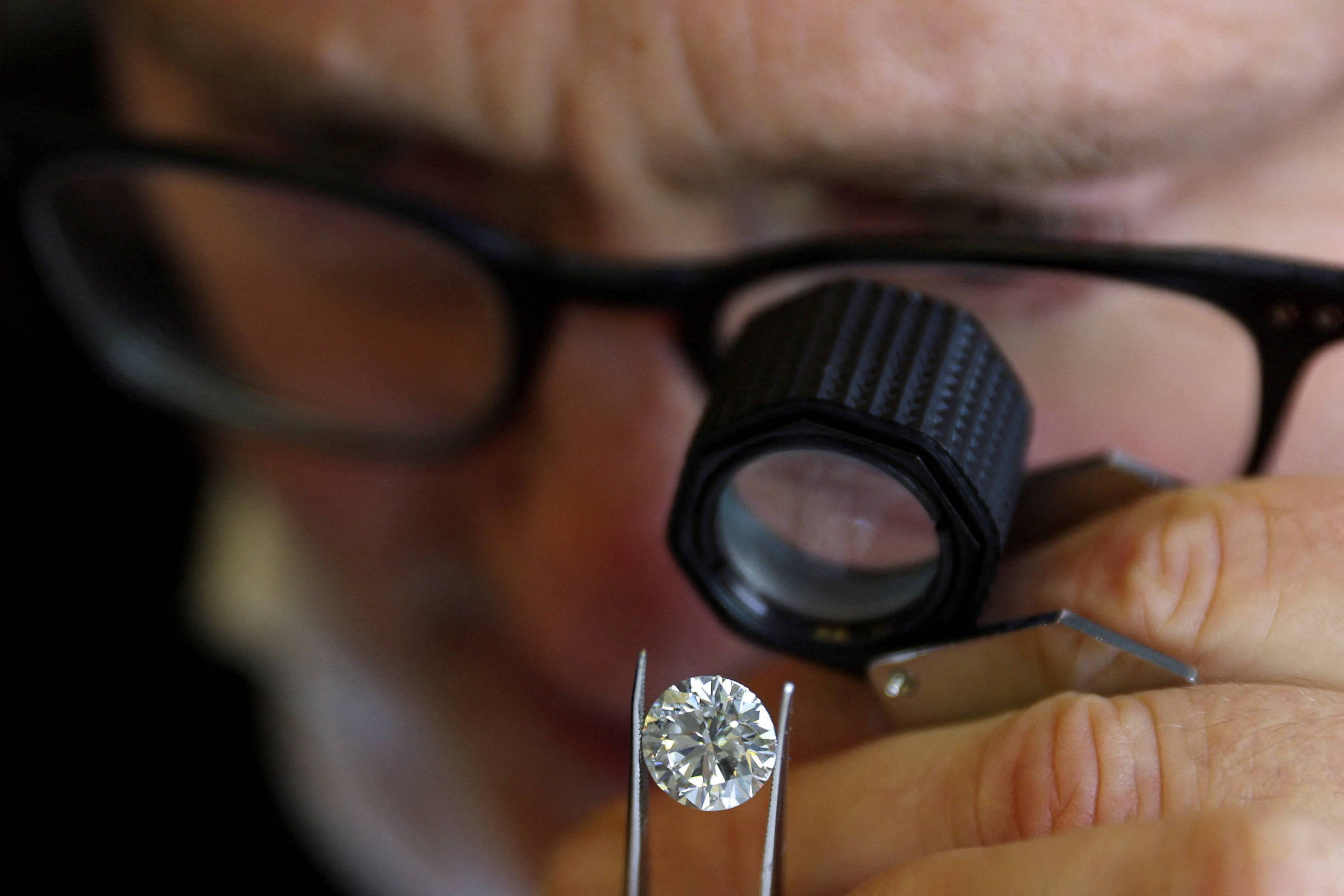 Diamantes laboratoriais ganham mercado com preços acessíveis e dominam na China Especialista inspecionando um diamante na Antuérpia (Foto: Johanna Geron - 30.out.23/Reuters)
