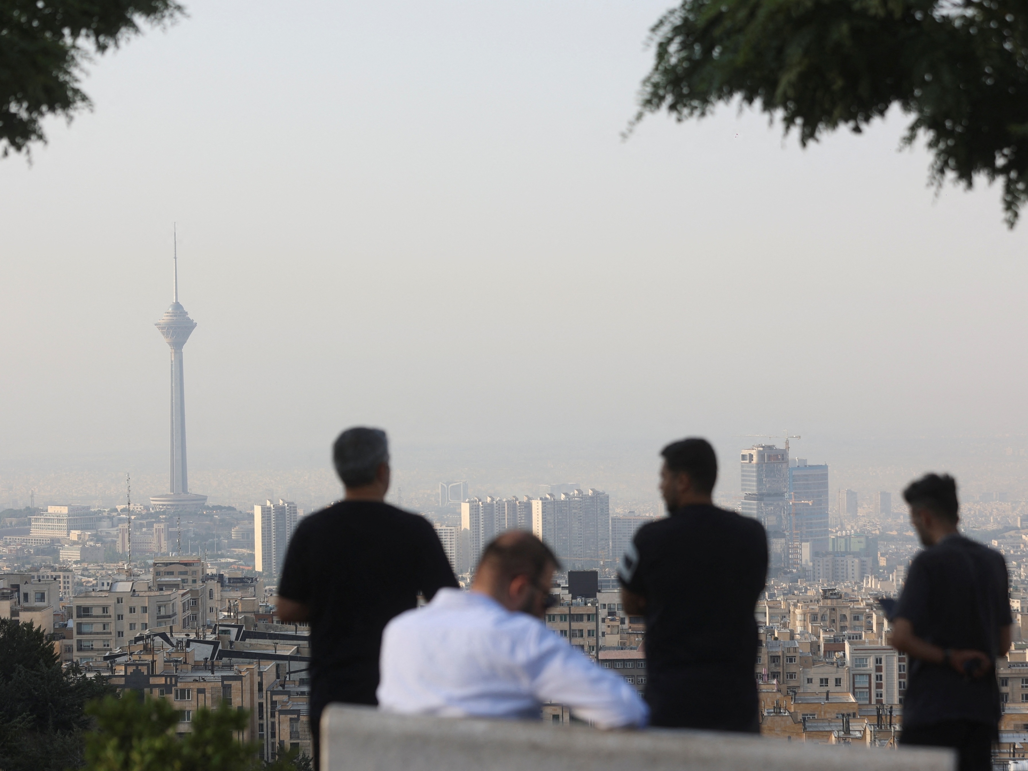 Homens observam a paisagem urbana após os ataques israelenses em Teerã, Irã (Foto: Majid Asgaripour/WANA via REUTERS)