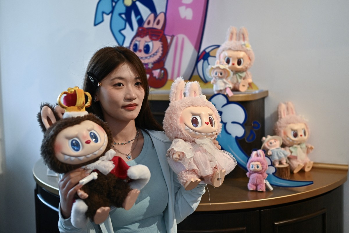 Mulher posando com os personagens Labubu (E) e Mokoko em um salão de exposições enquanto visita o parque temático Pop Land da Pop Mart, em Pequim (Foto: PEDRO PARDO / AFP)