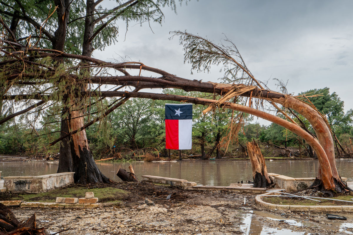Arte se mobiliza após enchentes no Texas e evento da Christie’s destaca tecnologia Uma bandeira do Texas pende de uma árvore danificada pela tempestade nas margens do rio Guadalupe em 13 de julho de 2025, em Center Point, Texas. (Foto: Brandon Bell/Getty Images)