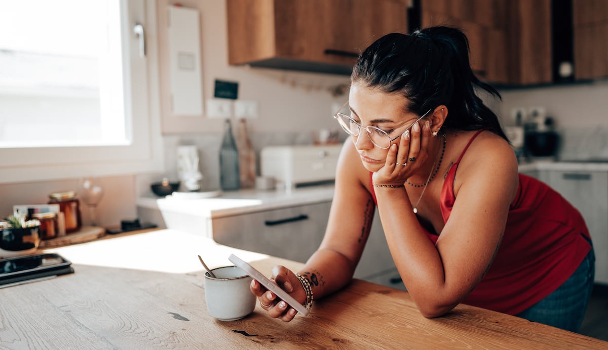 Uma mulher revisa seu smartphone na cozinha. (Foto: franckreporter/Getty Images)