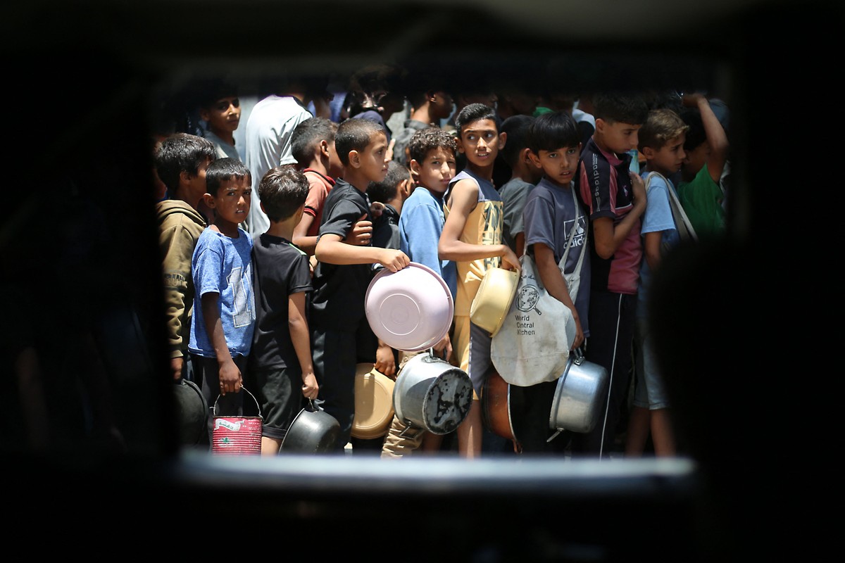 Crianças palestinas fazem fila para receber comida em um ponto de distribuição em Nuseirat, no centro da Faixa de Gaza (Foto: Eyad Baba/AFP)