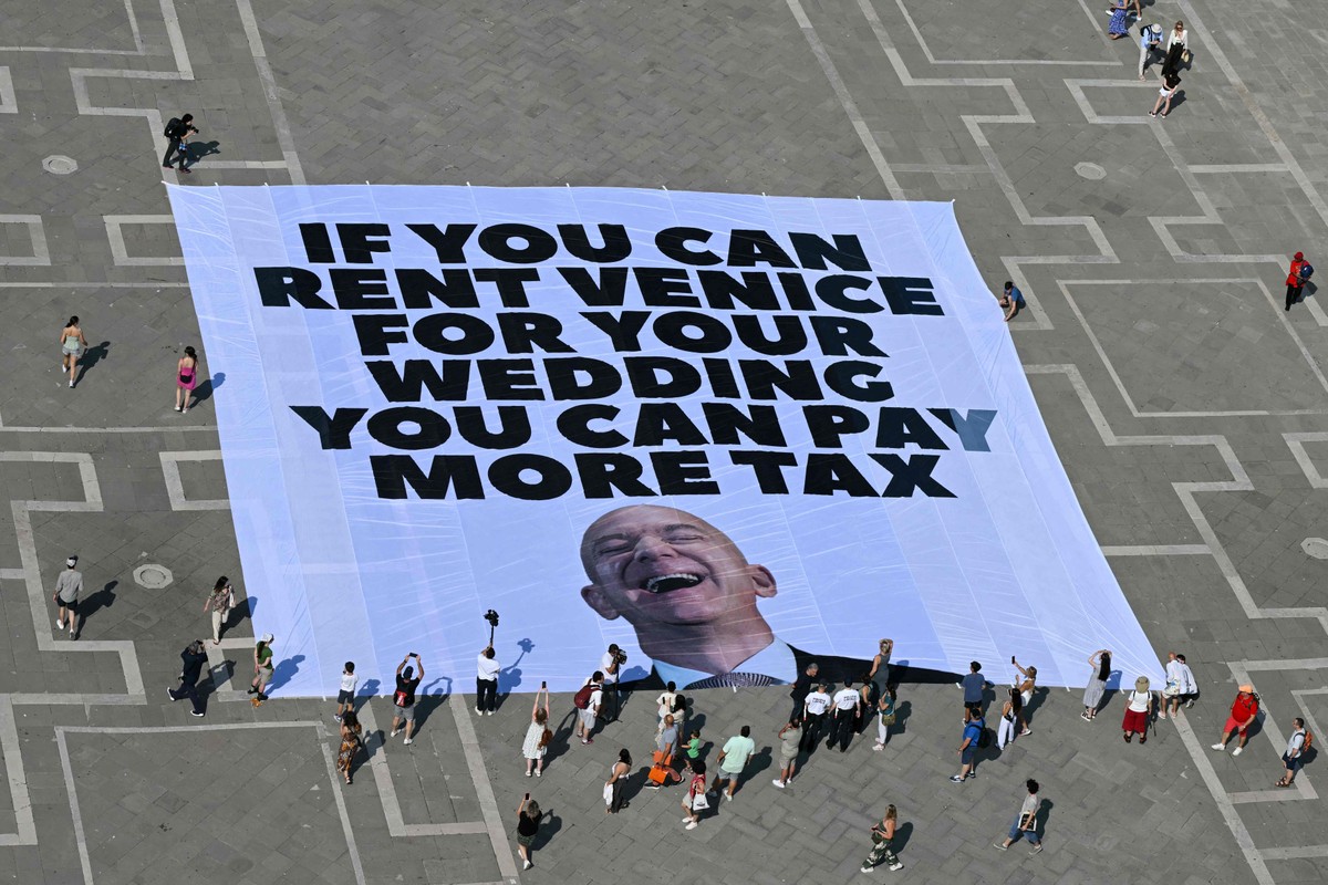 Protestos em Veneza marcam casamento milionário de Jeff Bezos e mudam local da festa Ativistas do grupo ambiental internacional Greenpeace exibem uma faixa gigante com uma foto de Jeff Bezos e os dizeres: “Se você pode alugar Veneza para seu casamento, você pode pagar mais impostos.” (Foto: Stefano Rellandini / AFP)