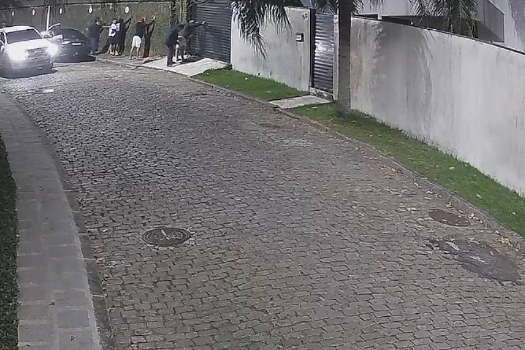 Polícia é atacada enquanto amigo de rapper Oruam estava rendido, afirma defesa Delegado Moyses Santana revista jovens antes de ataque ter início; defesa diz que Willyam Matheus Vieira estava rendido (bermuda branca) (Foto: Reprodução/Câmera de segurança)