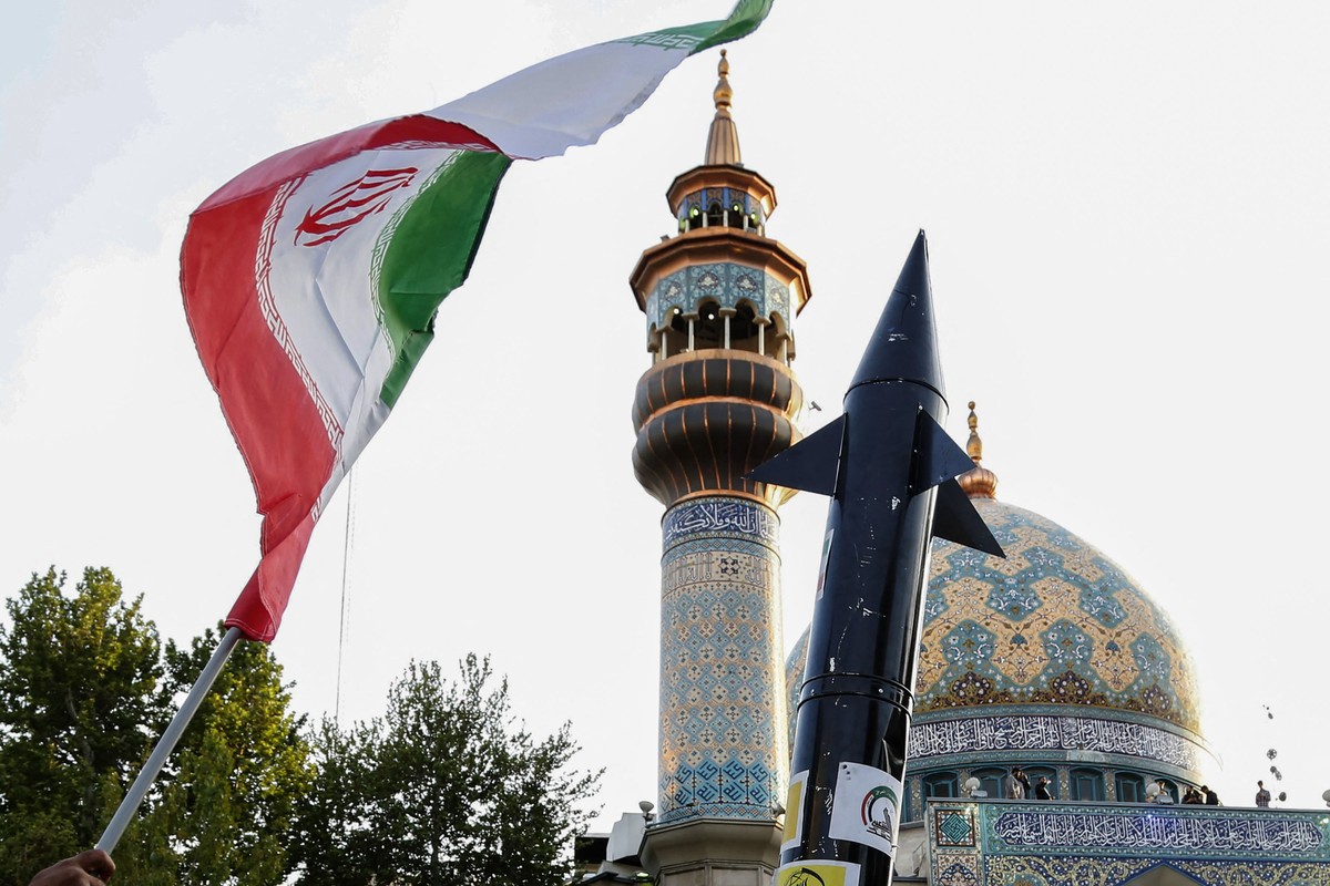 Iranianos levantam uma bandeira e a simulação de um míssil durante uma celebração após o ataque de mísseis e drones do Irã a Israel (Foto: AFP)