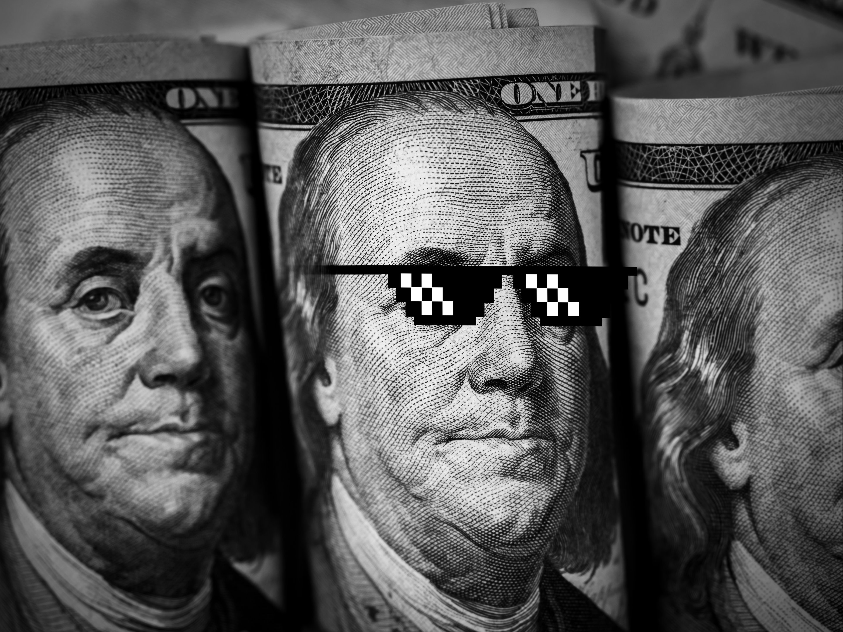 Investidores impulsionam alta das 'meme stocks' e aumentam apetite por risco Close-up do retrato do rosto de Benjamin Franklin usando óculos escuros pixelados engraçados em uma nota de 100 dólares, em preto e branco. Dinheiro, histórico financeiro. Notas de cem dólares. (Foto: Techa Tungateja/Getty Images)
