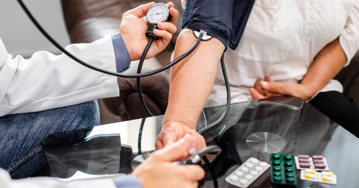 Três em cada dez hipertensos seguem tratamento, apesar de 90% afirmarem que sim Braço sobre uma mesa usando um aparelho de medir a pressão. Os braços de uma pessoa de jaleco manipulam o aparelho. Alguns comprimidos estão sobre a mesa. (Foto: USP Imagens)