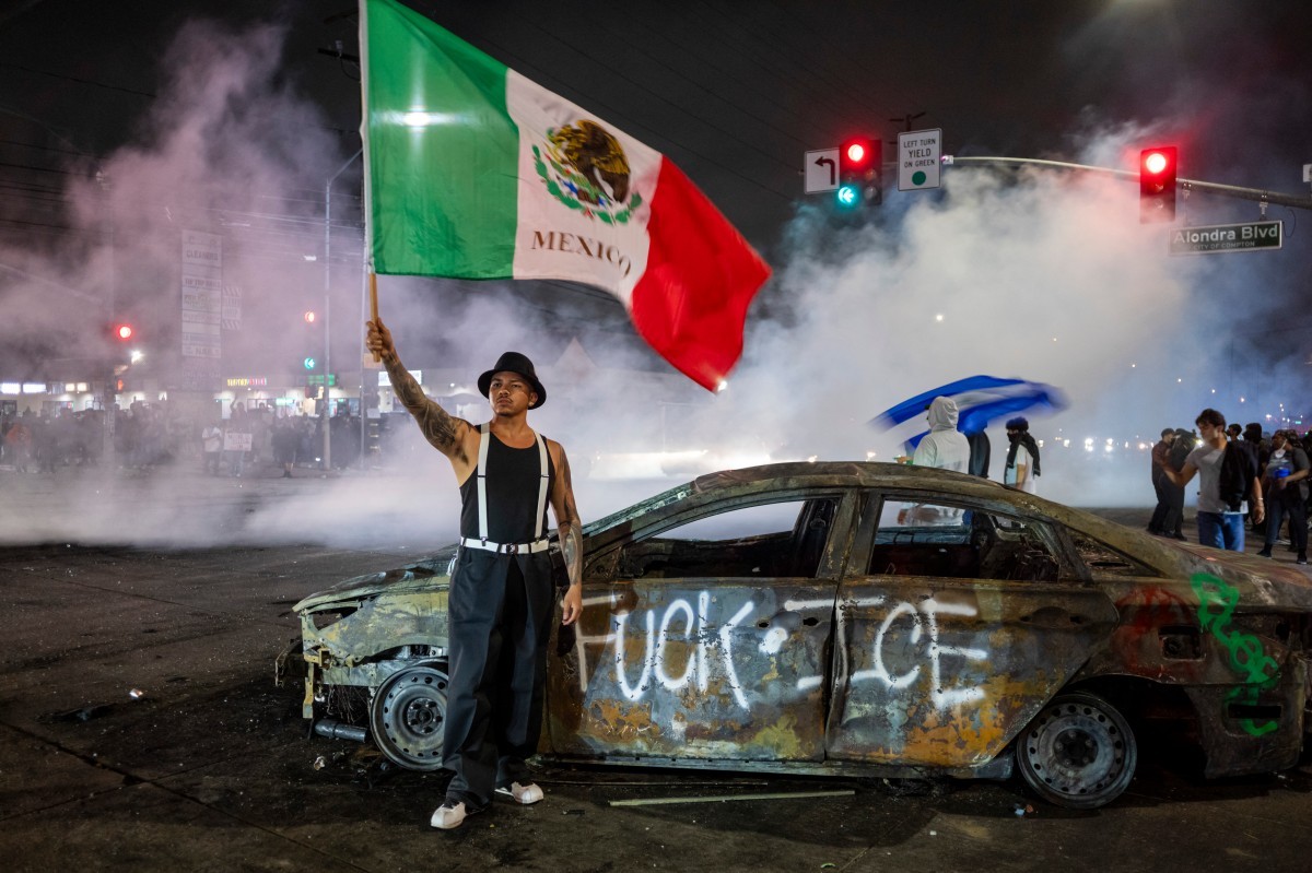 Manifestante segura bandeira do México em frente a pichação contra o Serviço de Imigração e Alfândega dos EUA (ICE, na sigla em inglês) em Los Angeles (Foto: RINGO CHIU / AFP)