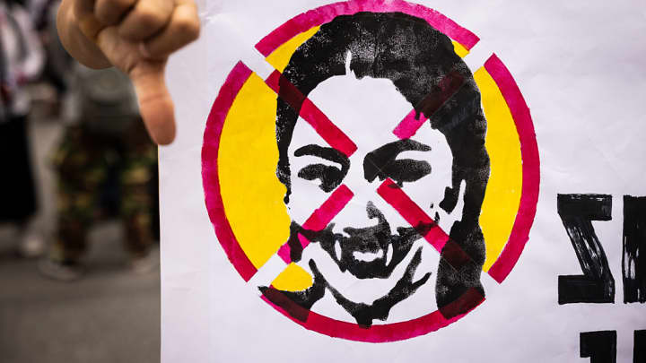 Crise política na Tailândia ameaça recuperação do turismo e da economia local Protesters hold a sign with a photo of Prime Minister Paetongtarn Shinawatra crossed out at Victory Monument on June 28, 2025 in Bangkok, Thailand. Thousands of protesters gathered at Bangkok’s Victory Monument to demand Prime Minister Paetongtarn Shinawatra resign over a leaked phone call linked to a border dispute with Cambodia. It was the largest anti-government rally since 2023, adding pressure ahead of a possible no-confidence vote. (Foto: Lauren Decicca | Getty Images News)