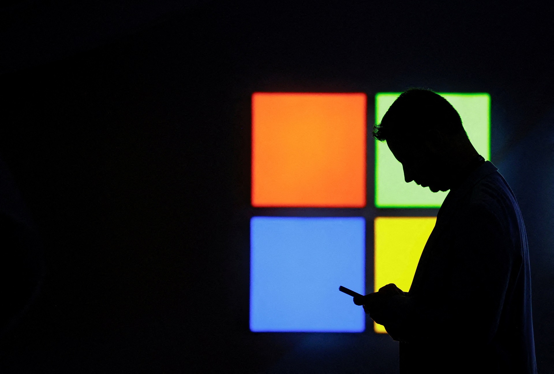 Um homem olha para o celular ao passar pelo estande da Microsoft na feira Mobile World Congress, em Barcelona, ​​Espanha, em 3 de março de 2025. (Foto: REUTERS/Bruna Casas/Foto de arquivo)