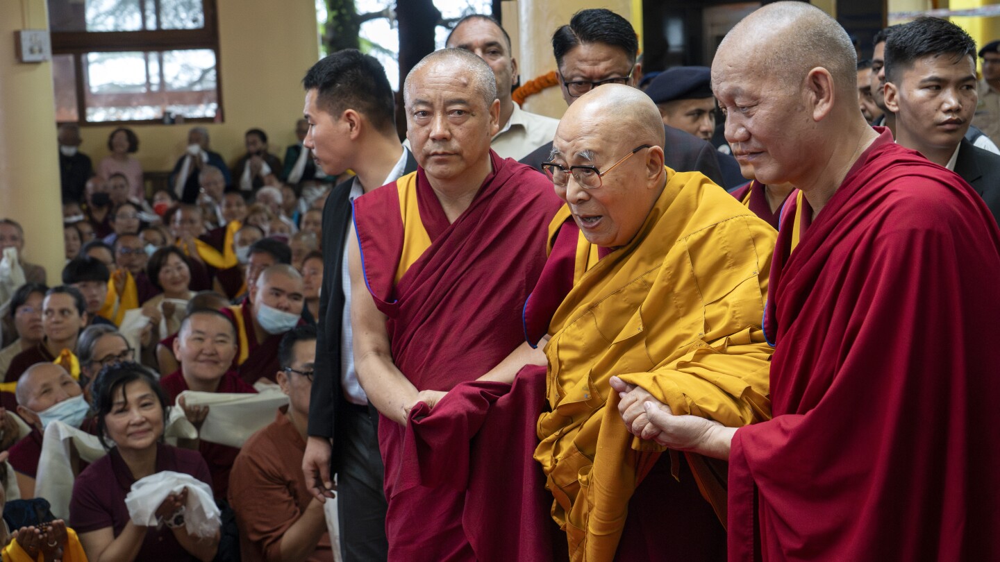 Líder espiritual tibetano, o Dalai Lama, em robe amarelo, é ajudado por monges assistentes ao chegar para presidir um evento durante o qual exilados tibetanos rezaram por sua longevidade, um dia antes de seu 90º aniversário, em Dharamshala, Índia, sábado, 5 de julho de 2025. (Foto: AP Photo/Ashwini Bhatia)