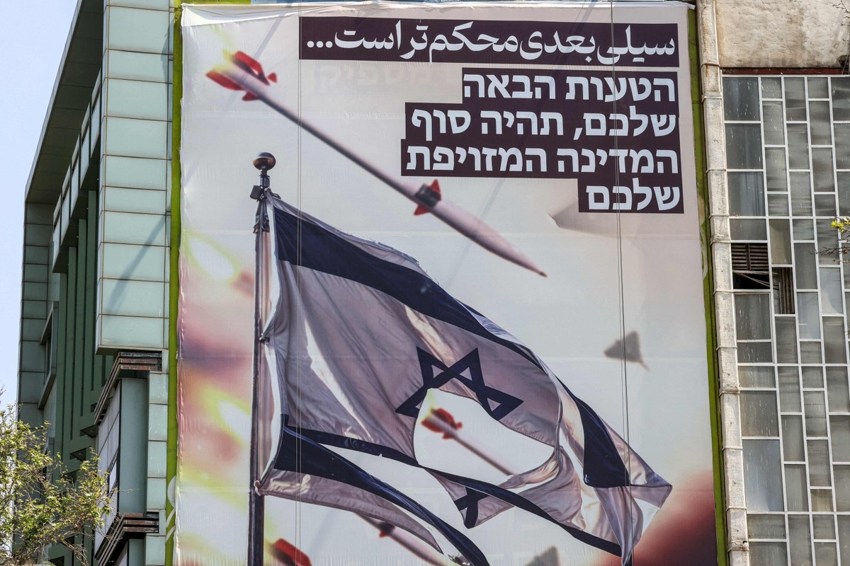Painel ilustrado na Praça Palestina, em Teerã, mostra mísseis e drones voando perto de uma bandeira israelense rasgada, dizendo, em farsi, 'o próximo tapa será mais violento' e, em hebraico, 'seu próximo erro será o fim de seu falso Estado' (Foto: ATTA KENARE / AFP)
