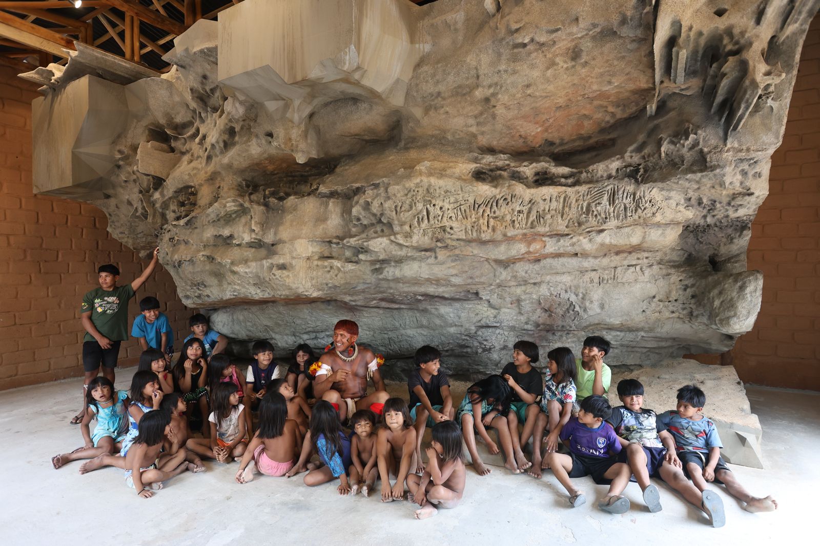 Cacique Akari Waurá cercado de crianças em frente à réplica da Gruta de Kamukuwaká (Foto: Alaor Filho/Fotos públicas)