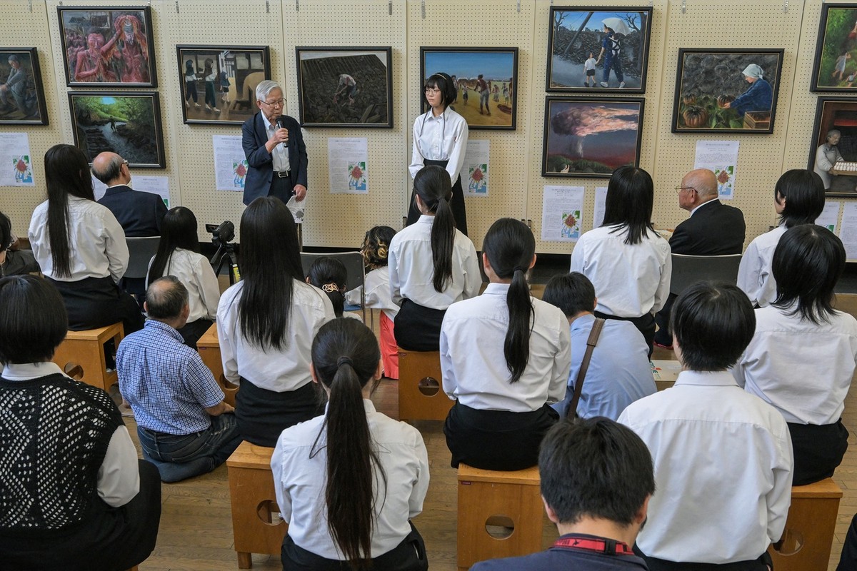 Adolescentes de Hiroshima expressam o trauma da bomba atômica por meio da arte Shingo Naito (em pé), sobrevivente da bomba atômica, na Escola Secundária Motomachi, em Hiroshima, em meio a pinturas criadas por alunos a partir de depoimentos de sobreviventes para manter as memórias do bombardeio de 1945 (Foto: RICHARD A. BROOKS / AFP)