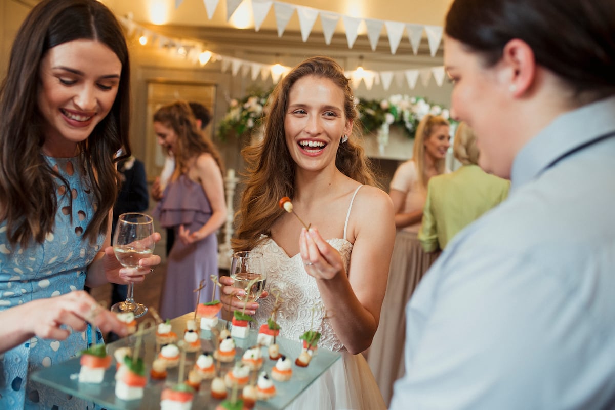 Uma noiva sorri enquanto pega um canapé no coquetel de seu casamento. (Foto: Getty Images)
