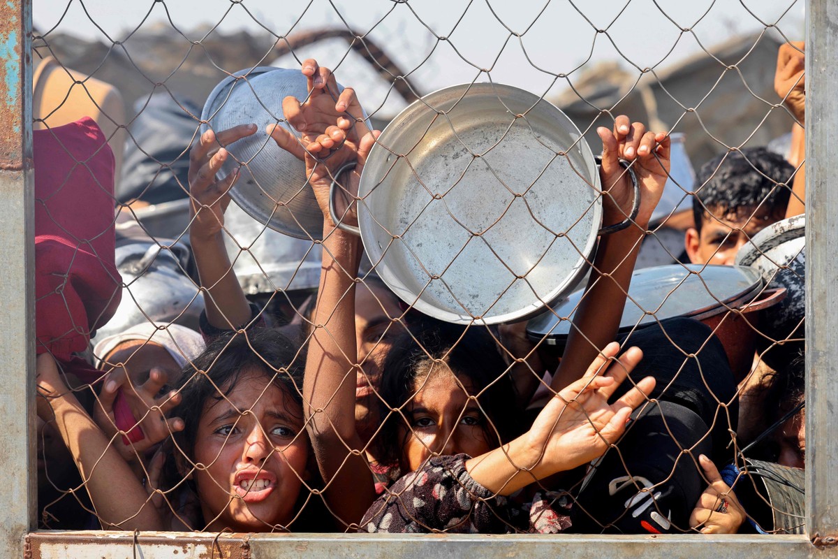 Gaza enfrenta crise humanitária com bloqueios e aumento da fome entre a população Crianças palestinas imploram por comida em área de ajuda humanitária próxima a Khan Younis, na Faixa de Gaza, em 22 de julho de 2025 (Foto: AFP)