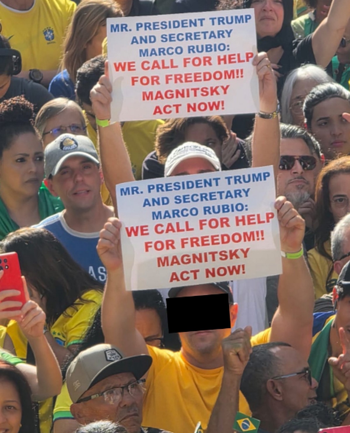 Foto de bolsonaristas erguendo cartazes em inglês pedindo a Donald Trump e Marco Rubio sanções dos EUA contra Alexandre de Moraes foi compartilhada por Eduardo Bolsonaro (PL-SP) e outros bolsonaristas omitindo rosto de manifestante nas redes sociais (Foto: Reprodução)