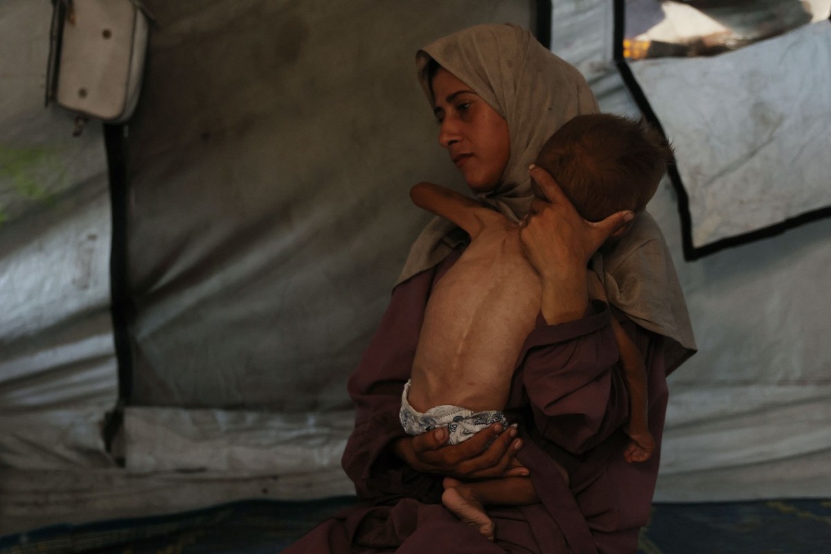 Hidaya, mãe palestina de 31 anos, segura seu bebê doente de 18 meses, Mohammed al-Mutawaq, que também tem sinais de desnutrição, dentro de sua tenda no campo de refugiados de Al-Shati, a oeste da Cidade de Gaza — Foto: Omar AL-QATTAA / AFP