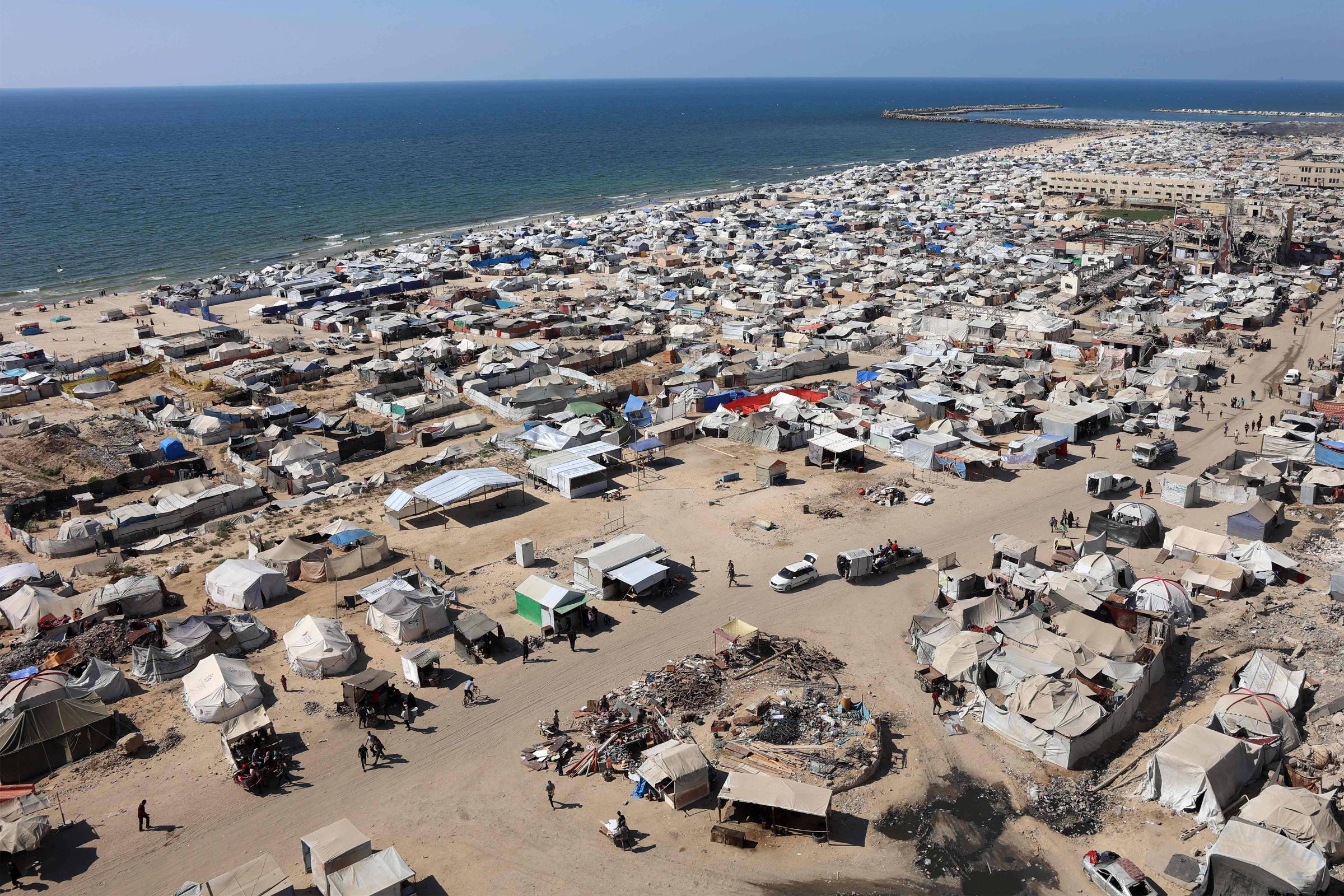 Tendas e abrigos de palestinos deslocados pelo conflito são vistos em um acampamento improvisado montado na praia, próximo ao porto de Gaza (Foto: Omar Al-Qattaa - 19,jul.25/AFP)
