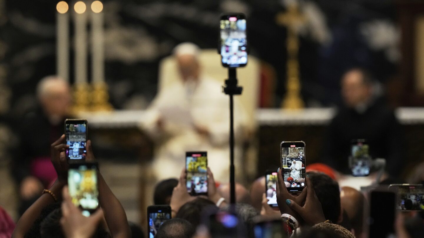 Fiéis filmam com seus celulares o Papa Leão XIV entregando sua mensagem ao final de uma missa celebrada pelo Cardeal Luis Antonio Tagle na Basílica de São Pedro, por ocasião do Jubileu da Juventude no Vaticano, na terça-feira, 29 de julho de 2025. (Foto: Gregorio Borgia/AP)