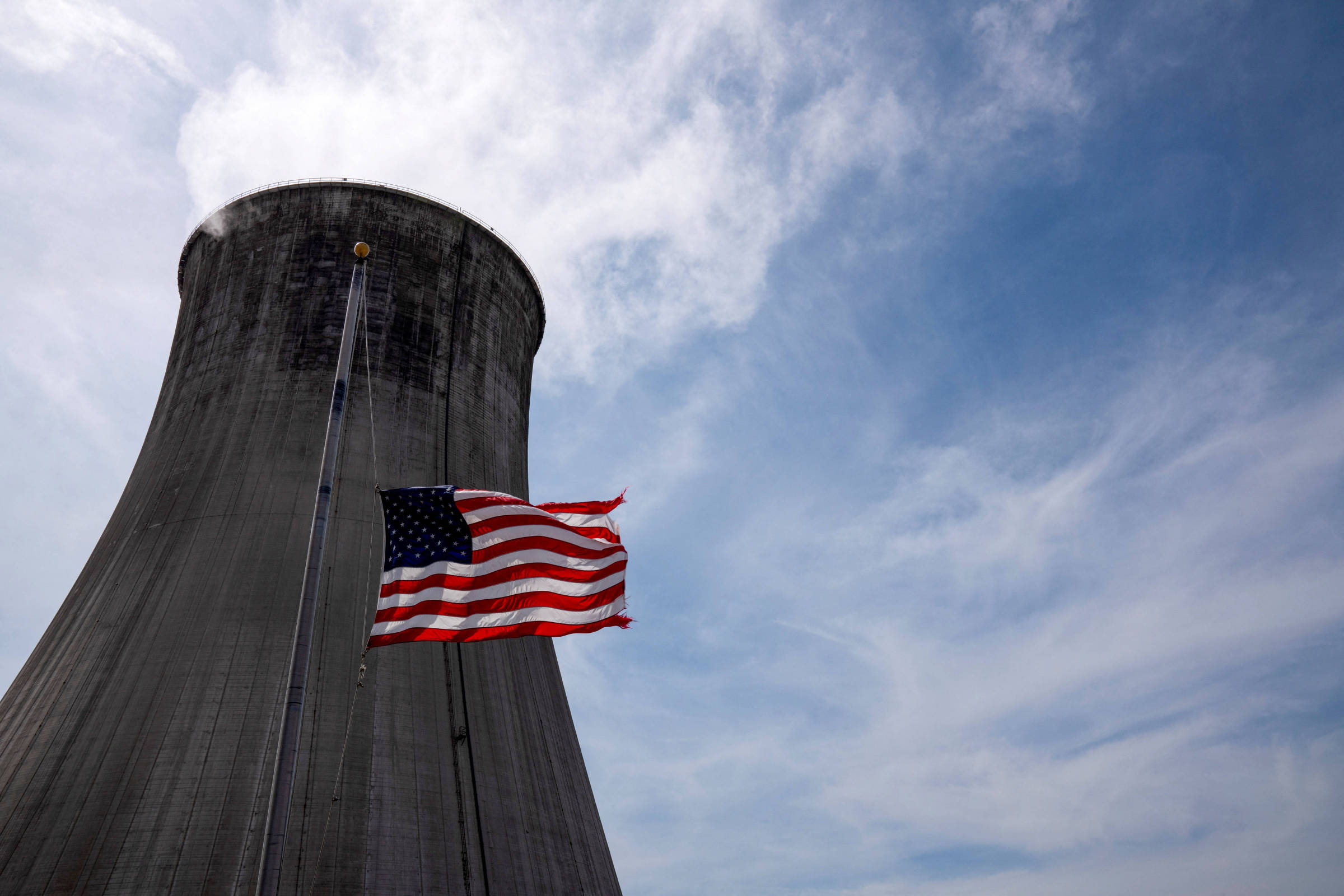 Bandeira americana tremula a meio mastro em frente à torre de resfriamento de uma usina termelétrica a carvão (Foto: Dane Rhys - 26.mar.21/Reuters)