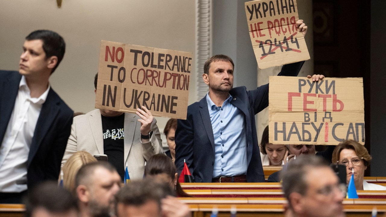 Parlamentares ucranianos protestam com cartazes com os dizeres como 'Sem tolerância à corrupção' e 'A Ucrânia não é a Rússia' durante votação para substituir lei que restringia órgãos anticorrupção em Kiev. 31/07/2025 (Foto: Andrii Nesterenko/AFP)