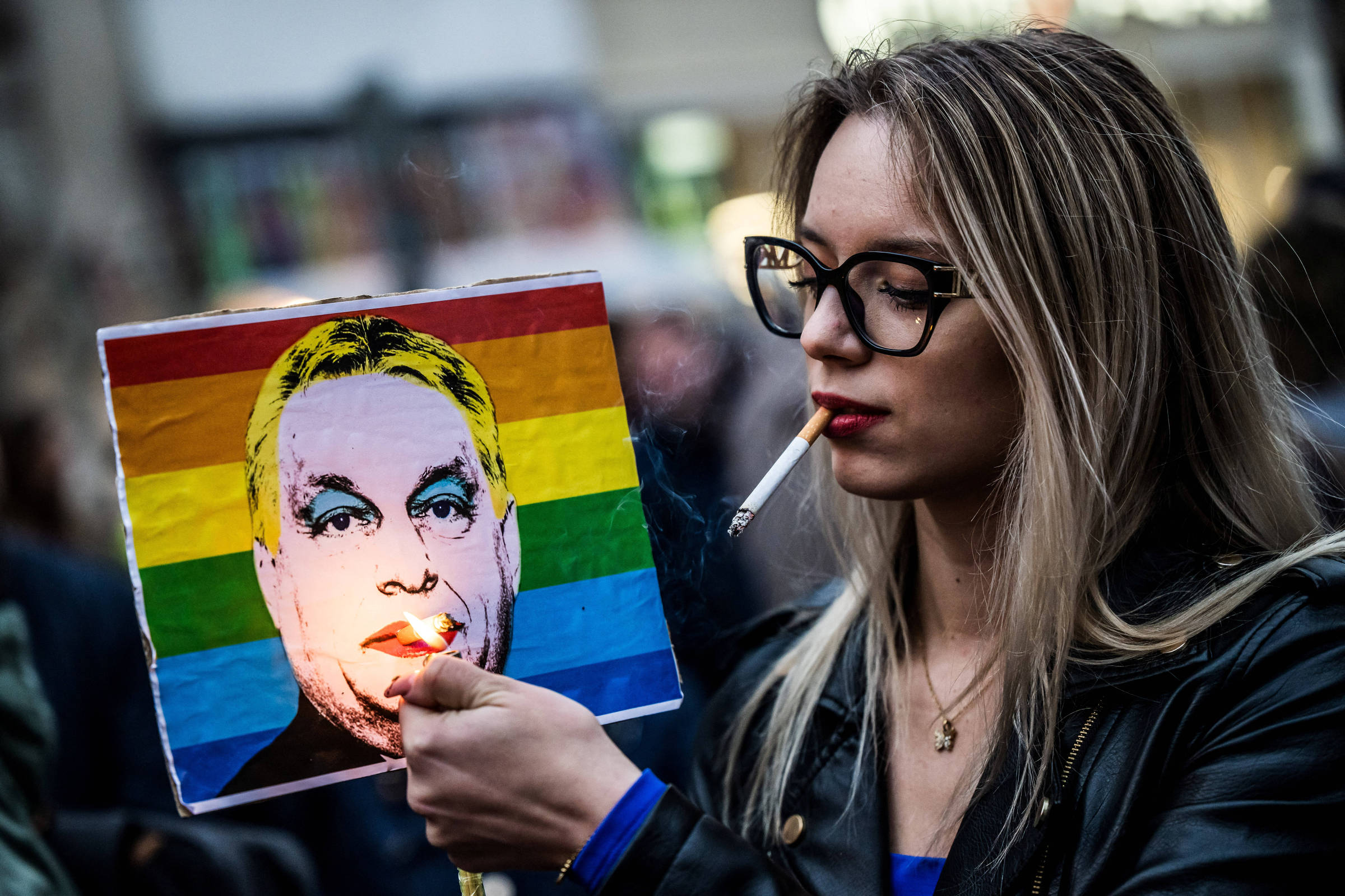 Parada LGBTQ+ na Hungria se torna ato de resistência contra governo de Orban Mulher acende cigarro em cartaz representando o primeiro-ministro Viktor Orbán após o Parlamento húngaro aprovar uma lei que proíbe a comunidade LGBTQIA+ de realizar a marcha do orgulho (Foto: Marton Monus - 25.mar.2025/Reuters)