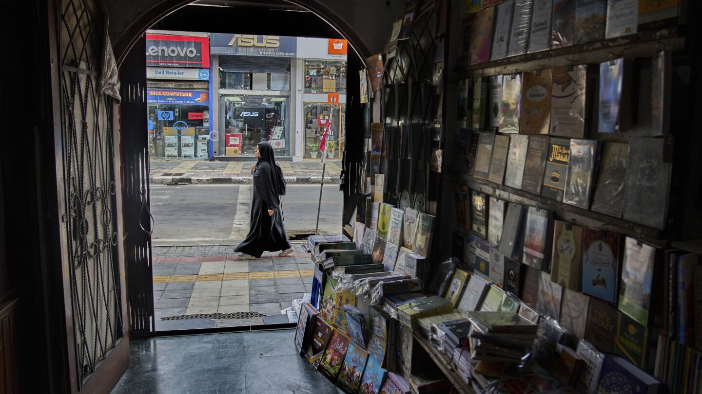 Uma mulher do Caxemira passa por uma livraria em Srinagar, controlada pela Índia, na quinta-feira, 7 de agosto de 2025. (Foto: AP Photo/ Dar Yasin)