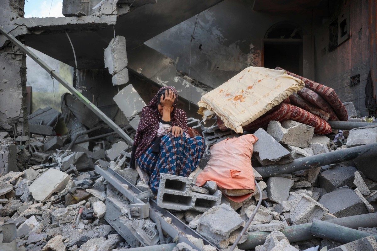 Mulher palestina chora sentada nos escombros de sua casa, destruída no ataque israelense contra o campo de refugiados de Nuseirat (Foto: Eyad Baba/AFP)