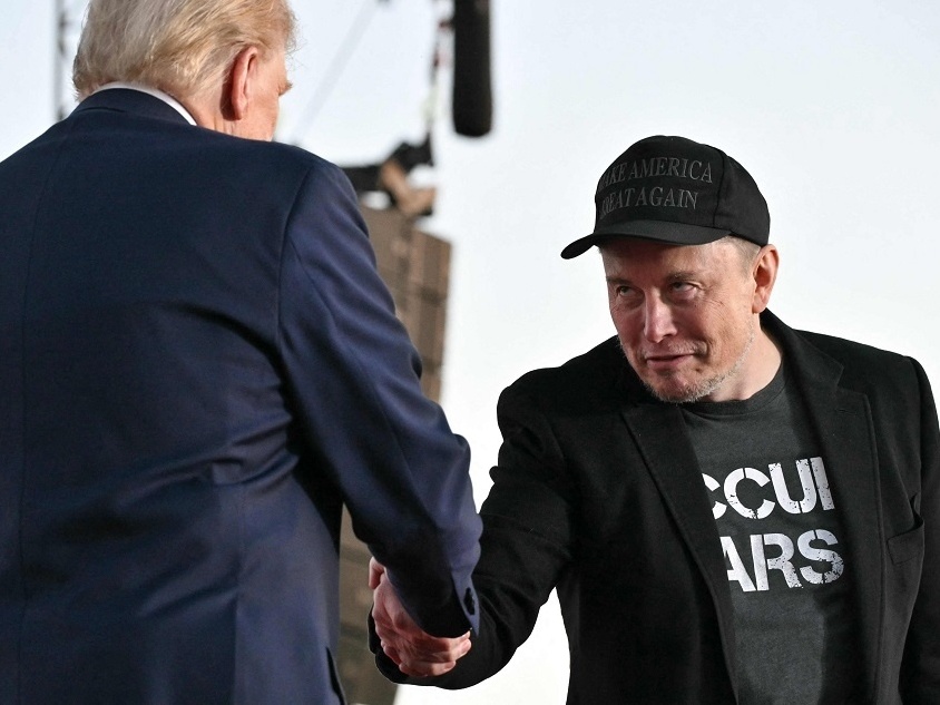 Elon Musk cumprimenta Donald Trump em evento oficial de campanha (Foto: Jim WATSON / AFP)