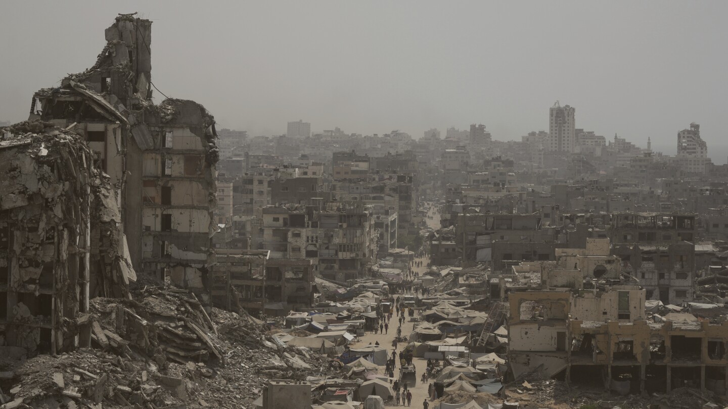Pessoas caminham ao longo de uma rua ladeada por edifícios destruídos após bombardeios israelenses durante a guerra Israel-Hamas na Faixa de Gaza, terça-feira, 29 de julho de 2025. (Foto: AP Photo/Jehad Alshrafi)