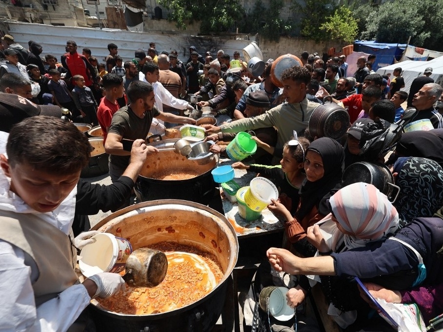 Palestinos fazem fila para receber uma porção de comida quente no campo de refugiados de Nuseirat, no centro da Faixa de Gaza (Foto: Eyad Baba / AFP)