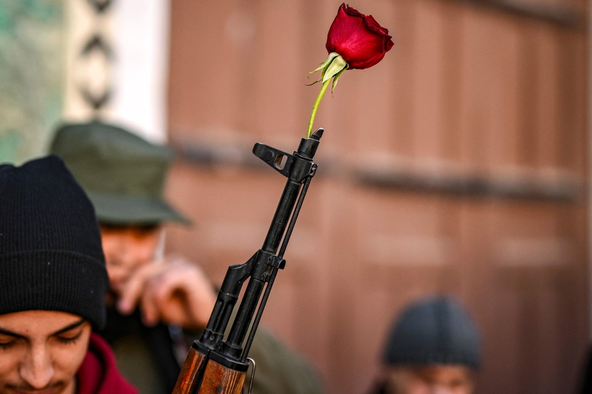 EUA retiram designação de 'terrorista' de grupo rebelde sírio que assumiu o poder Uma rosa é colocada em um rifle de um combatente rebelde sírio antes das orações semanais muçulmanas de sexta-feira na mesquita Umayyad, em Damasco (Foto: Aris MESSINIS / AFP)