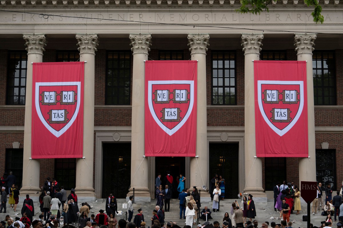 Bandeiras com o símbolo de Harvard adornam um dos prédios da universidade que se tornou símbolo da resistência da ciência aos ataques de Trump (Foto: AFP)