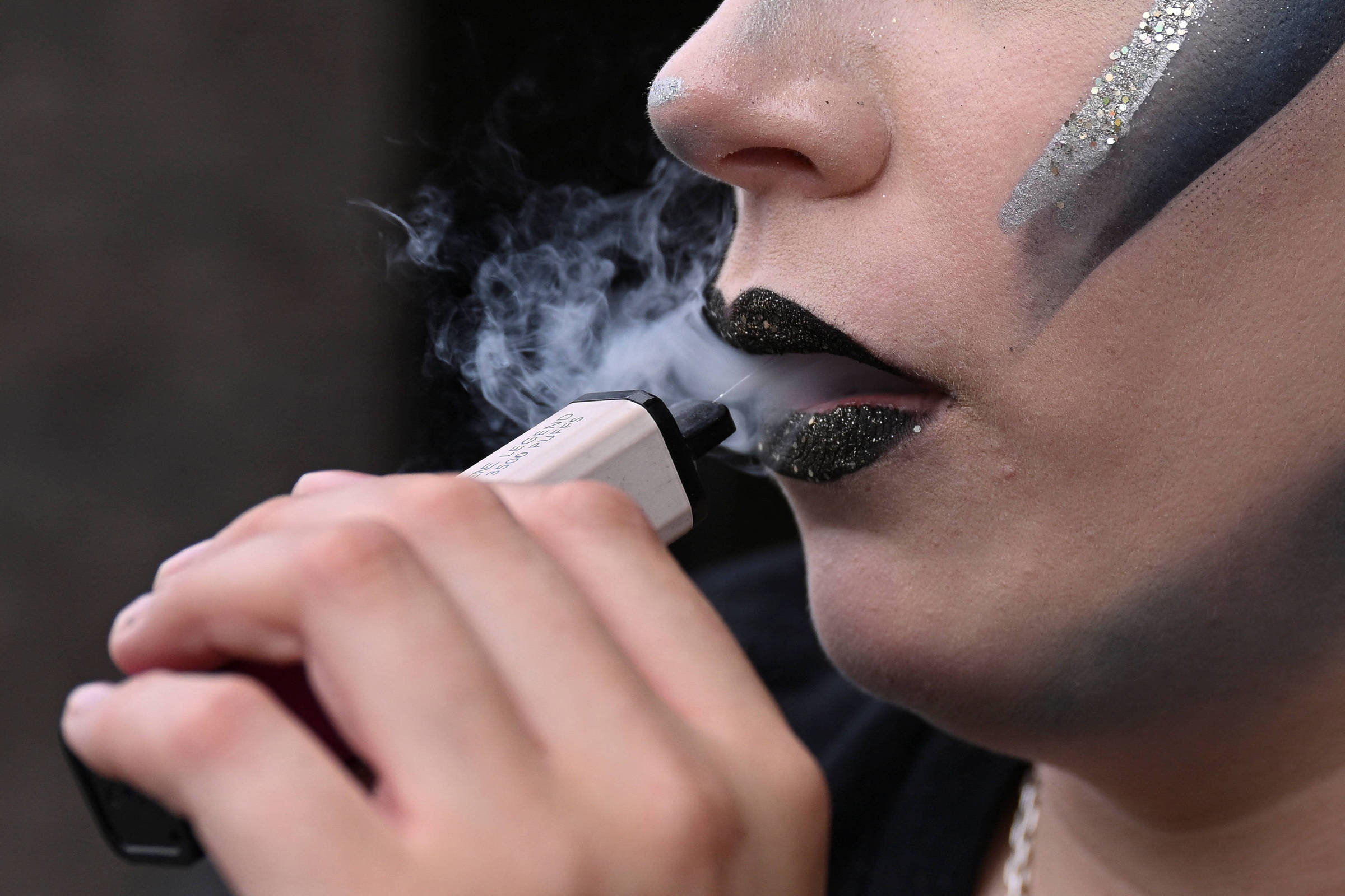 Jovem usa vape em entrada de teatro em Londres, na Inglaterra (Foto: Jaimi Joy - 31.mai.2025/REUTERS)