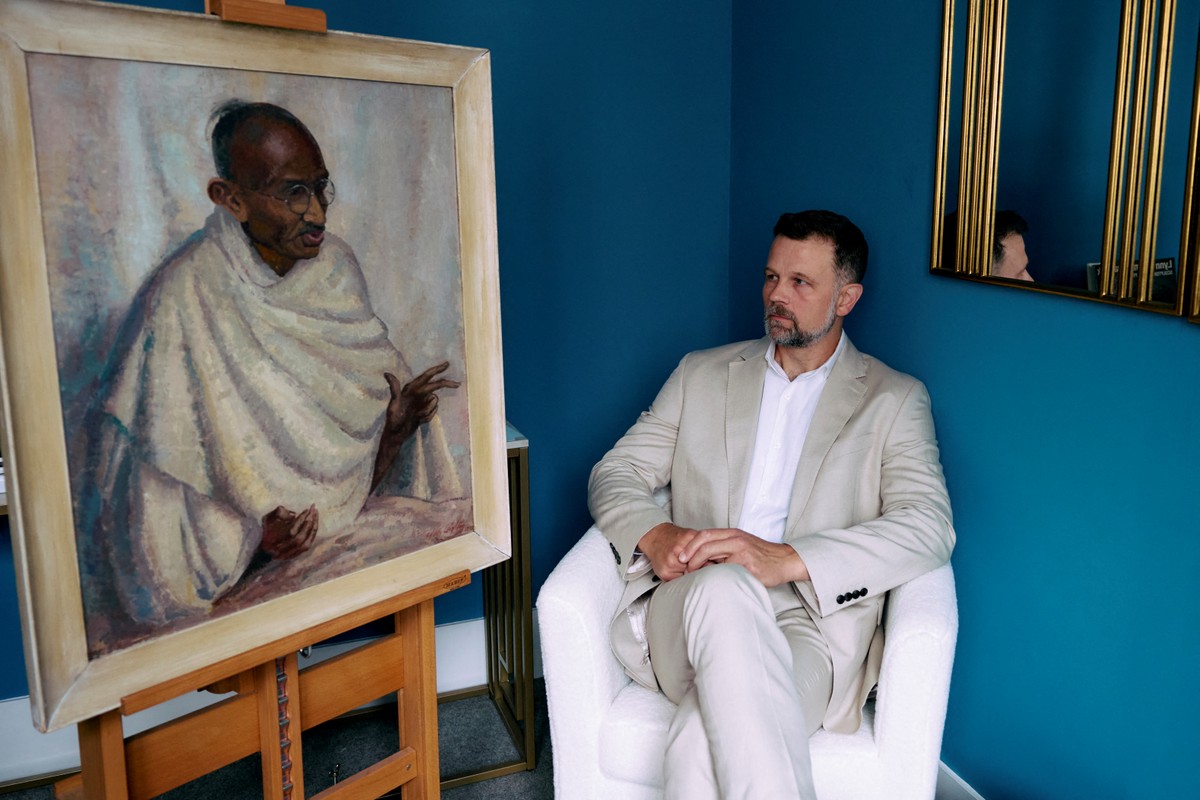 Caspar Leighton, sobrinho-neto da artista anglo-americana Clare Leighton, posa ao lado do retrato de Ghandi feito por sua tia-avó (Foto: BENJAMIN CREMEL / AFP)